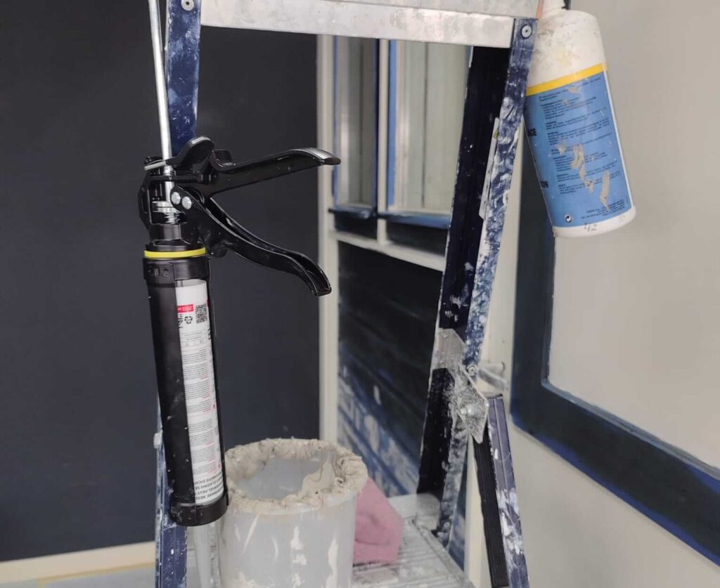 Voorbereiding voor het glaskitten op de vakschool: kitspuit en gereedschap op een trap