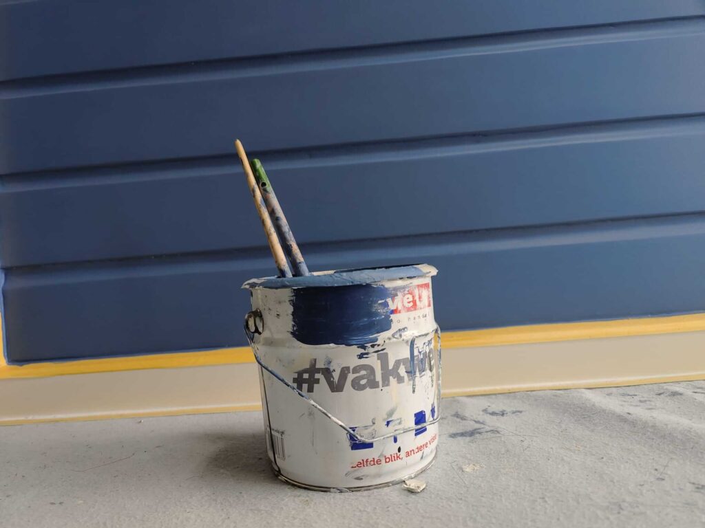 Pot blauwe verf met twee kwasten en geschilderde blauwe rabatdelen