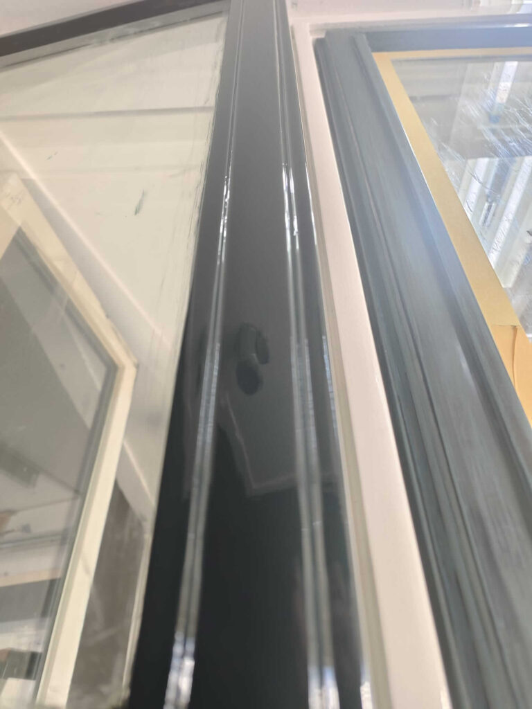 Detail van een strak afgelakt raam op de vakschool, waarbij de glans van de synthetische verf goed zichtbaar is.